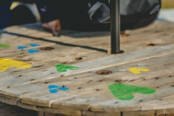 Gros plan sur une table fabriquée avec une grosse roue en bois, sur laquelle les chevrons de la STM sont peints en jaune, vert et bleu