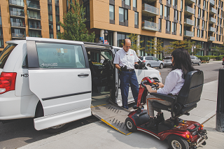 1.	The driver of an accessible taxi welcomes a passenger, who is using a four-wheel mobility scooter.