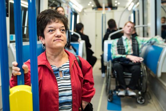 Photo dans une voiture d’un métro Azure d’une petite personne qui se tient sur la barre de soutien à l’avant-plan et d’un homme en fauteuil roulant dans la zone réservé à l’arrière-plan.