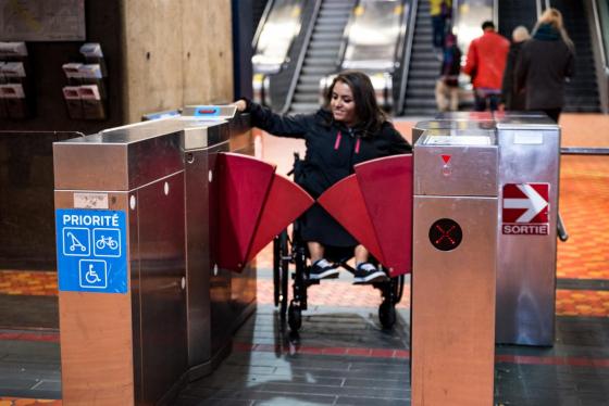 Photo d’une femme en fauteuil roulant qui valide sa carte OPUS aux portes-papillon d’une station de métro. 