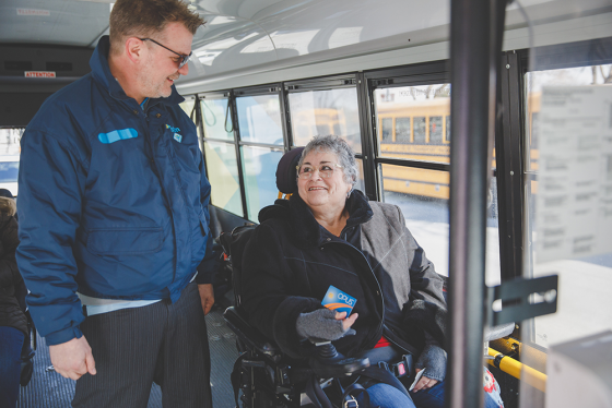 Photo chauffeur transport adapté qui aide une cliente en fauteuil roulant à bord d'un bus T A.